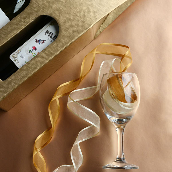 Gold double wine box alongside wine glass filled with satin edge sheer ribbons spilling out.